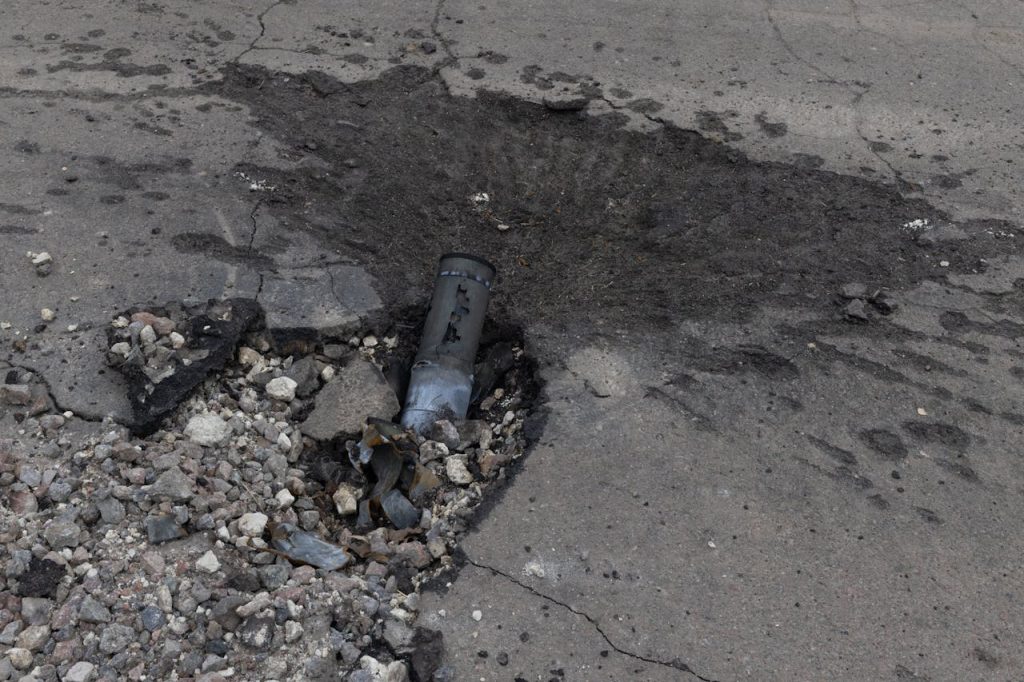 Aged asphalt road showing severe damage and debris from an explosion impact.